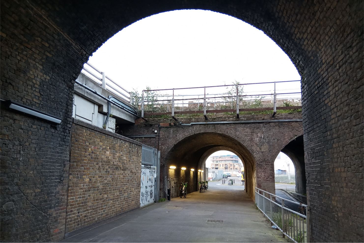 An arch unde a railway bridge looking out from another railway arch.